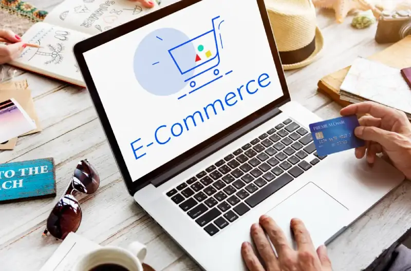 Migrinfo - Création de site e-commerce Ordinateur affichant un site e-commerce avec une personne tenant une carte bancaire